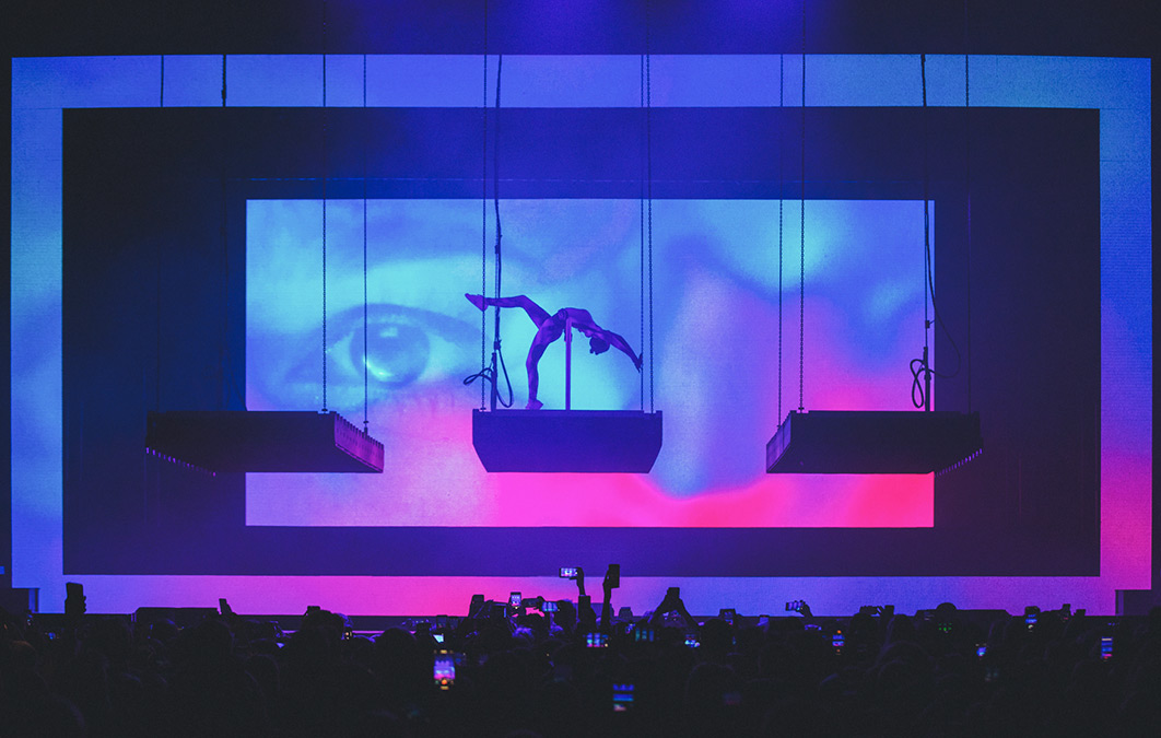 Acrobatic performer on small plinth dangled above crowd for concert